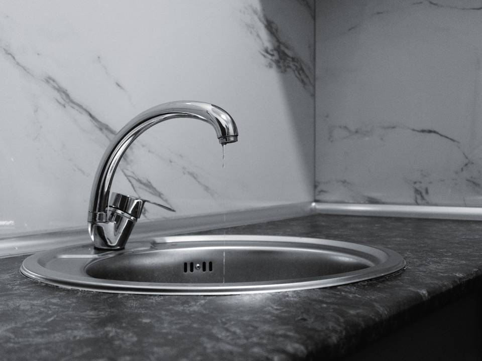 Torneira cromada pingando sobre uma pia de inox