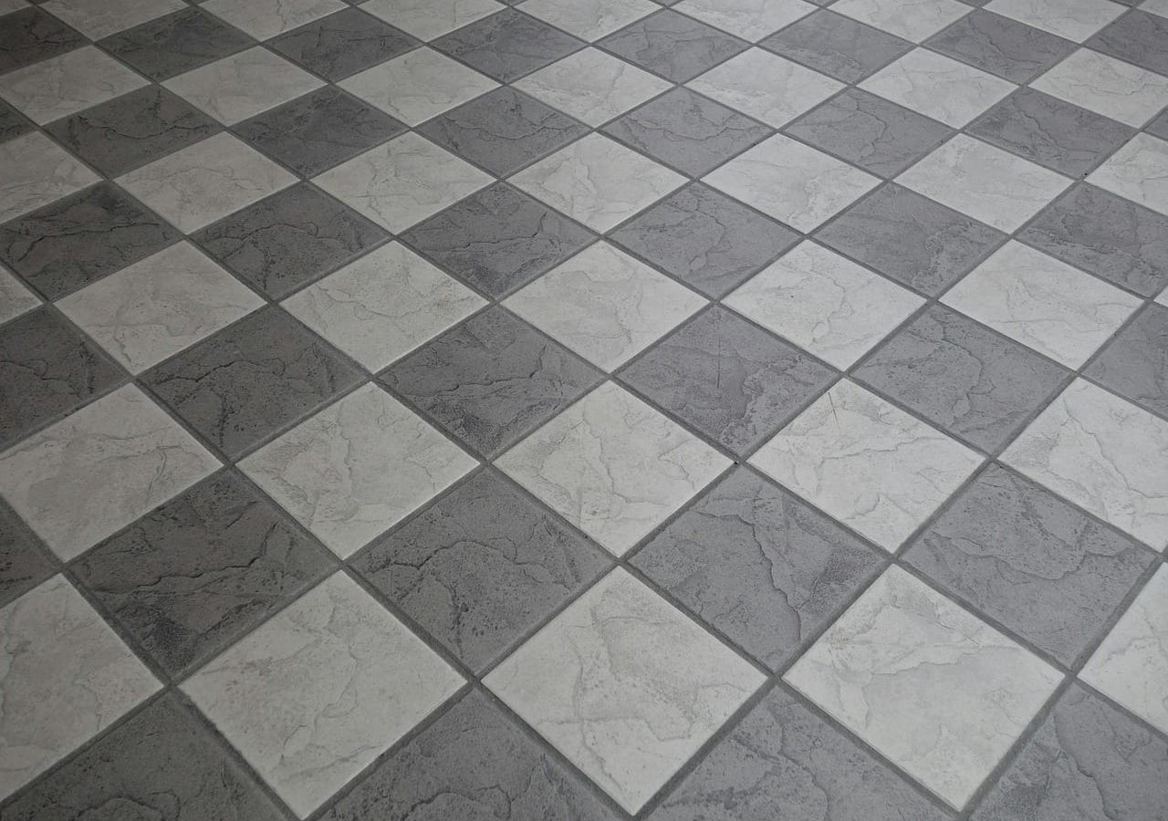 Piso revestido com cerâmicas cinzas e brancas dispostas em formato de xadrez.